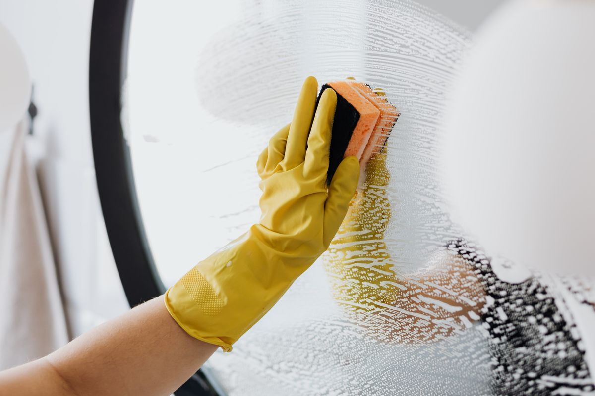 Cleaner in yellow gloves scrubbing a glass surface during a deep clean